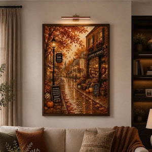 May include: A rectangular wall art print depicting a rainy autumn street scene with orange foliage, a street lamp, and a storefront labelled Coffee & Books. The scene includes pumpkins, fallen leaves, and signs with text including Happy Autumn.
