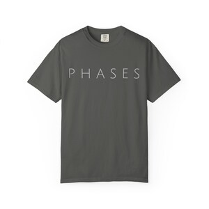 May include: Dark gray t-shirt with the word "PHASES" printed in a light gray color across the chest. The shirt has short sleeves and a crew neck. The fabric appears to be a soft cotton blend.