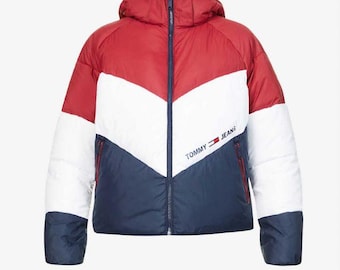 May include: A hooded puffer jacket in red, white, and navy blue. The jacket features a chevron design across the chest and the words "TOMMY JEANS" printed on the front. The jacket has a full zipper closure and two side pockets.