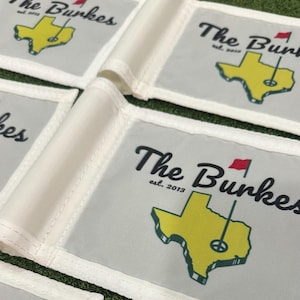 May include: Golf flags with the text "The Burkes est. 2013" in black script. The flags feature a yellow outline of Texas with a golf pin and red flag. The flags are white with a gray background.