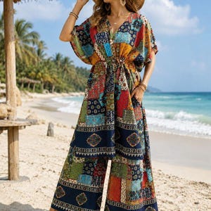 Op de afbeelding: Een tweedelige set bestaande uit een tuniek met V-hals, korte mouwen en een trekkoord in de taille, gecombineerd met een wijde broek. Het kledingstuk heeft een levendig, meerkleurig patchworkpatroon met bloemmotieven en geometrische vormen in blauw, rood en geel.