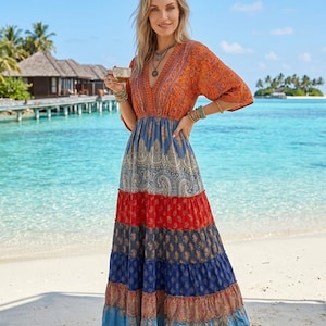 May include: A floor-length maxi dress featuring a deep V-neckline and elbow-length sleeves. The bodice is orange with a paisley pattern, while the skirt consists of horizontal tiers in alternating colors of blue, red, and light blue with paisley prints.