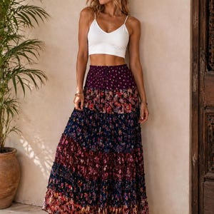 May include: A white sleeveless crop top with a V-neckline paired with a floor-length tiered maxi skirt. The skirt features a dark purple, navy blue, and burgundy floral print with a gathered, ruffled texture throughout the fabric layers.