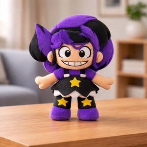 Könnte beinhalten: Plüschpuppe im Cartoon-Design. Die Puppe hat lila und schwarze Haare, ein lila Oberteil und einen schwarzen Rock mit gelben Sternen. Die Beine und Füße sind lila, und sie hat einen lächelnden Gesichtsausdruck.