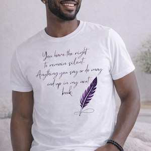 Puede incluir: Camiseta blanca con el texto "You have the right to remain silent. Anything you say or do may end up in my next book." y una ilustración de pluma morada. La camiseta la lleva una persona.
