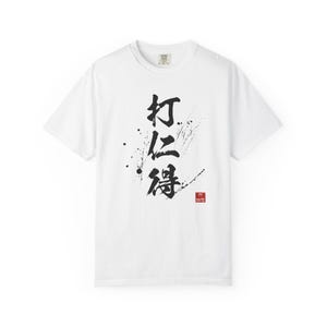May include: White t-shirt with a black calligraphy design and ink splatter. The design includes Chinese characters and a small red square with text. A casual, short-sleeved tee.