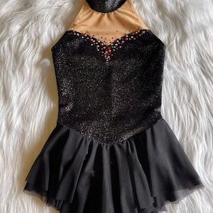 May include: Black figure skating dress with a sparkly bodice and a black tulle skirt. The bodice has a high neckline and a sheer panel with rhinestones and red accents.