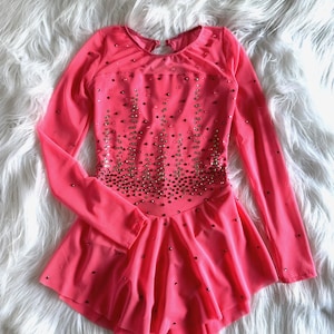 May include: A pink figure skating dress with long sleeves and a sparkly design. The dress has a fitted bodice and a flared skirt.
