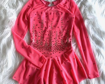 May include: A pink figure skating dress with long sleeves and a sparkly design. The dress has a fitted bodice and a flared skirt.