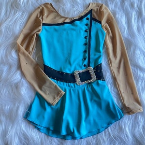 May include: A turquoise and black figure skating dress with long sleeves and a black belt with a large silver buckle. The sleeves are sheer and have a tan color. The dress has a ruffled skirt.