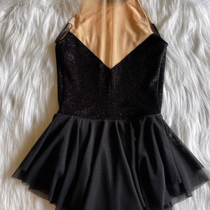 May include: Black dance leotard with a sheer mesh panel in the back and a black tulle skirt. The leotard has a sparkly finish.