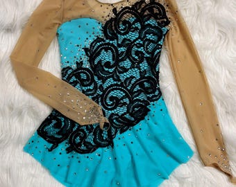 May include: A turquoise and black figure skating dress with long sleeves and a lace design. The dress is embellished with rhinestones.
