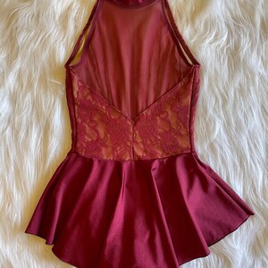 May include: Burgundy dance leotard with a lace bodice and a ruffled skirt. The leotard has a high neckline and a sheer back panel.