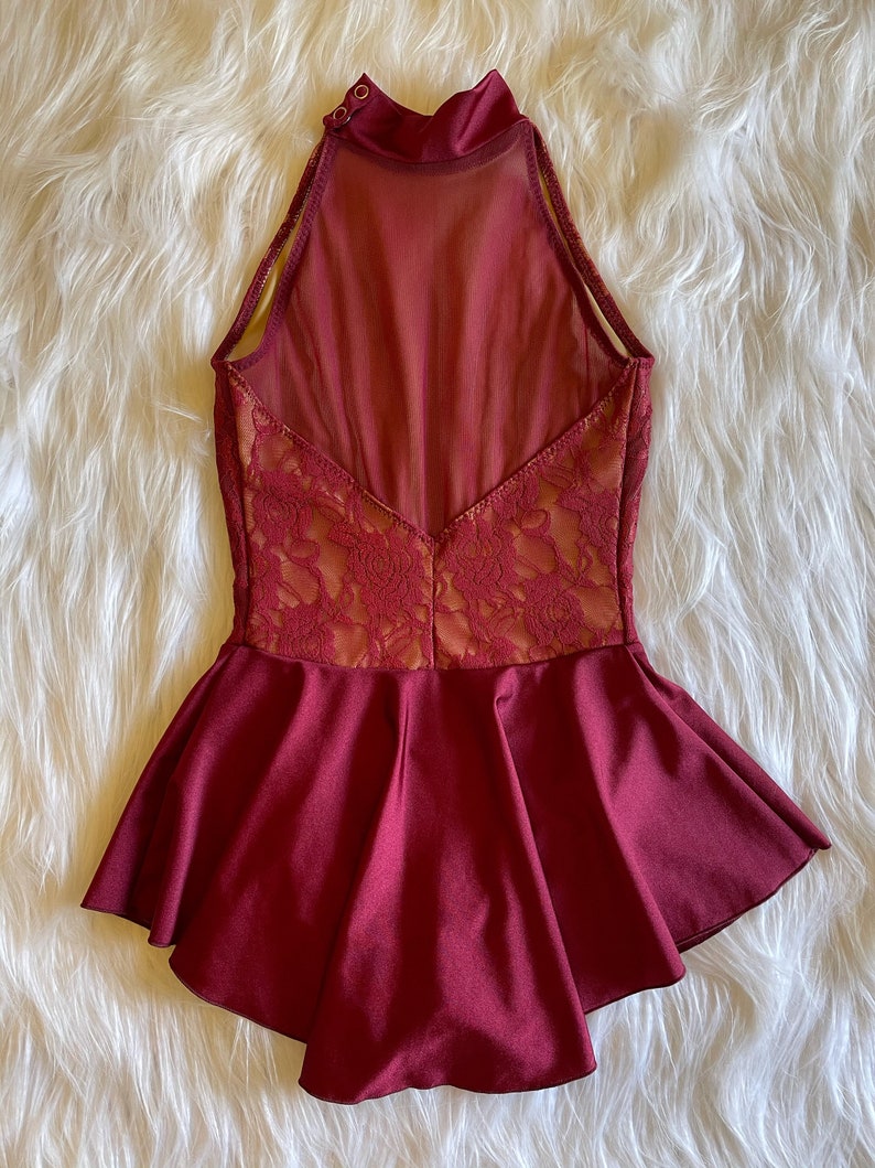 May include: Burgundy dance leotard with a lace bodice and a ruffled skirt. The leotard has a high neckline and a sheer back panel.
