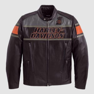 Puede incluir: Chaqueta de moto de cuero negro con el logotipo de Harley-Davidson en el pecho. La chaqueta presenta rayas naranjas y grises en las mangas y el pecho, y un pequeño parche en la parte superior del pecho. La chaqueta tiene cuello alto y bolsillos con cremallera.