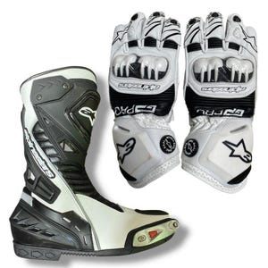 May include: White and black motorcycle boots and gloves. The boots are high-top with a white and black color scheme, featuring the brand name. The gloves are white with black accents and protective features, also displaying the brand logo.
