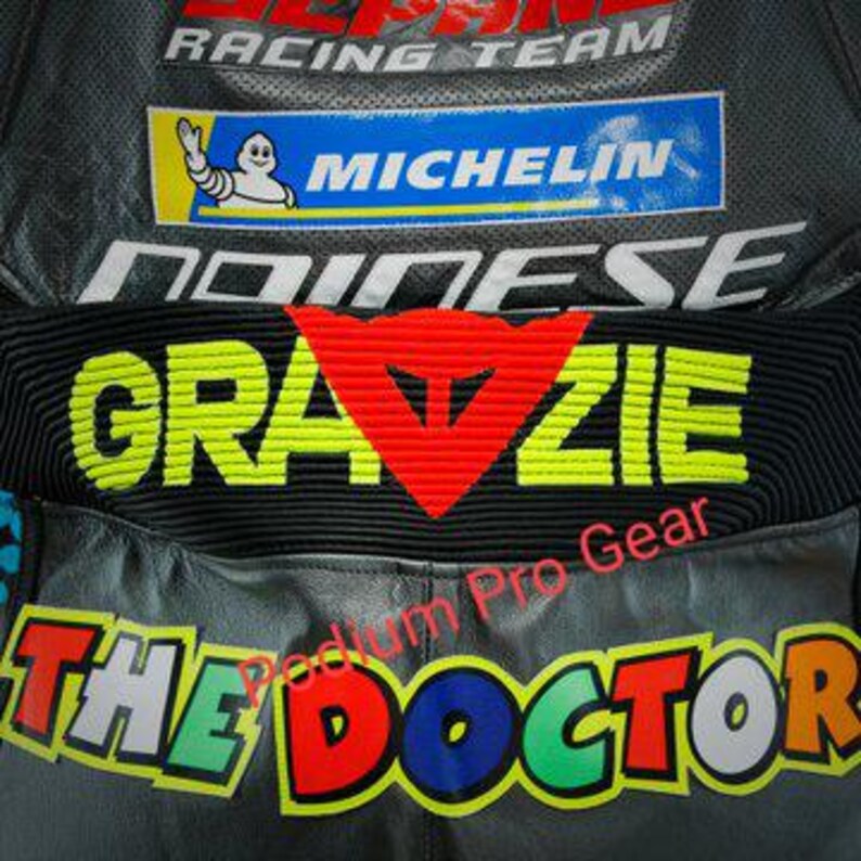 May include: A black leather motorcycle racing suit featuring the text GRAZIE in neon yellow, a red Dainese logo, and the text THE DOCTOR in multi-colored letters. The suit includes a blue Michelin logo and the text SEPANG RACING TEAM.