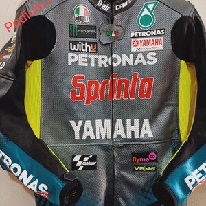 May include: A grey and black leather motorcycle racing jacket featuring perforated panels, neon yellow side accents, and various sponsor logos including Petronas, Yamaha, Monster Energy, AGU, and Sprinta. The text Podium Pro Gear is visible.
