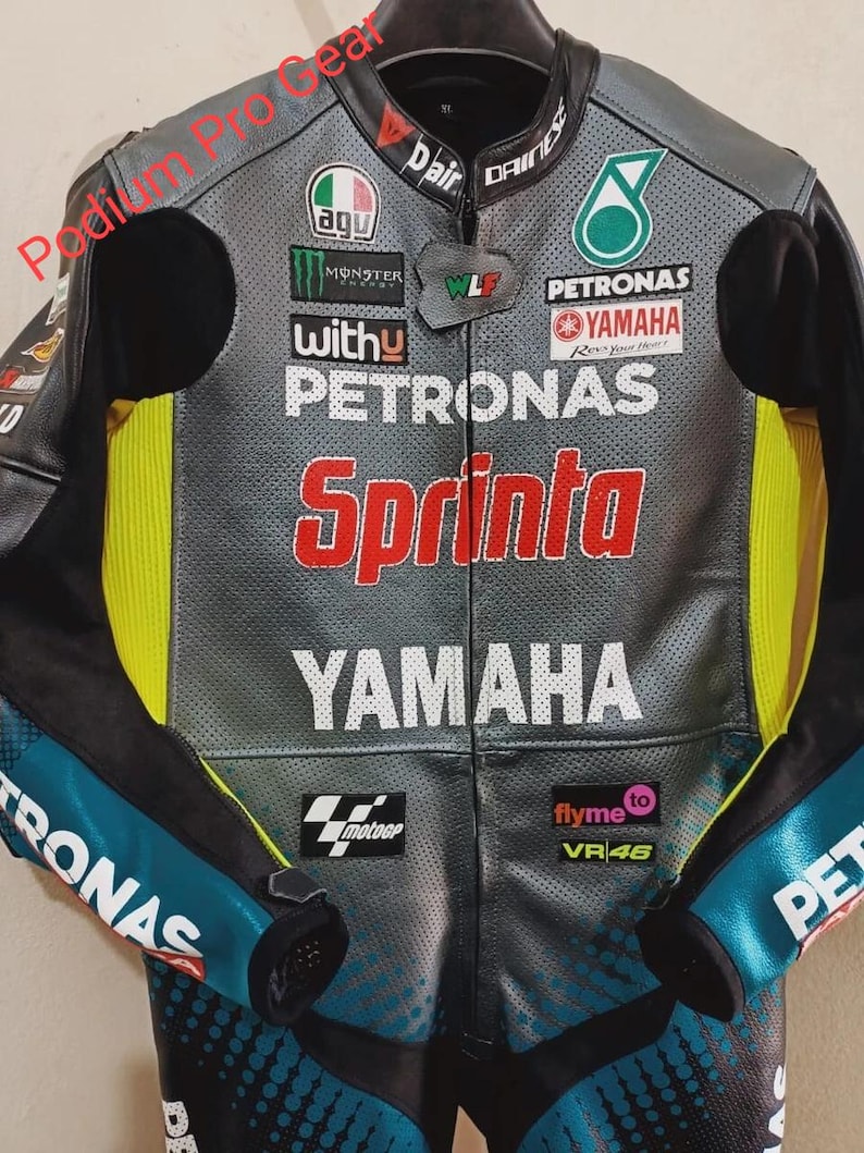 May include: A grey and black leather motorcycle racing jacket featuring perforated panels, neon yellow side accents, and various sponsor logos including Petronas, Yamaha, Monster Energy, AGU, and Sprinta. The text Podium Pro Gear is visible.