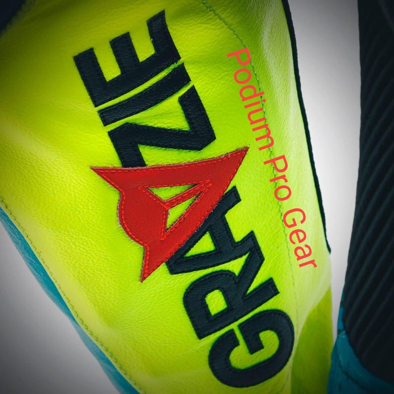 May include: A neon yellow leather motorcycle suit panel featuring the black text GRAZIE and a red triangular logo emblem. The text Podium Pro Gear is printed in red vertically along the side of the bright yellow leather surface.