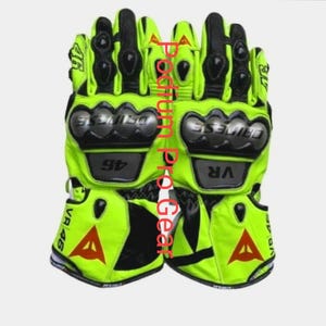 May include: A pair of neon yellow and black motorcycle gloves featuring hard knuckle protectors, the text VR 46, and a red triangular logo. The gloves display the Dainese brand name on the knuckle guards and include additional protective padding.