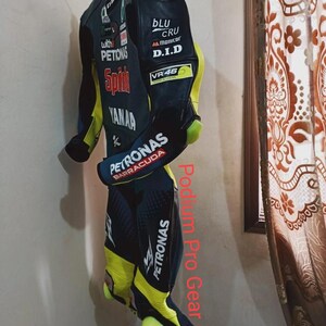 May include: A black, blue, and neon yellow motorcycle racing suit featuring various sponsor logos including Petronas, Yamaha, and VR46. The suit has protective shoulder caps, long sleeves, and full-length legs with integrated knee sliders.