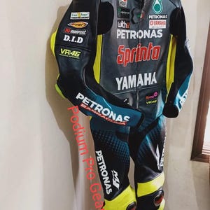 May include: A black, teal, and neon yellow leather motorcycle racing suit featuring multiple sponsor logos including Petronas, Yamaha, Sprinta, and VR46. The suit has a full-length front zipper, protective padding at the shoulders and knees.