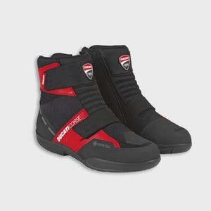 May include: Pair of black and red motorcycle boots featuring the Ducati Corse logo. The boots have a high-top design with Velcro straps and the Gore-Tex logo. Designed for motorcycle riding.