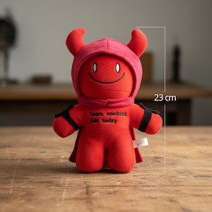 May include: A red plush devil doll, approximately 23 cm tall, with a hood, horns, and a cape. The doll has a smiling face and the text "team coolkidd join today" on its chest. Black bands are around the arms.