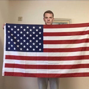 Peut inclure: Un grand drapeau américain avec 50 étoiles blanches sur un fond bleu et des rayures rouges et blanches alternées. Le drapeau rectangulaire est tenu par une personne.