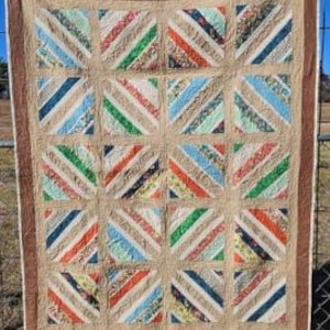 May include: A handmade quilt with a patchwork design. The quilt features a grid of squares, each filled with diagonal stripes in various colors including blue, green, orange, and beige. The quilt is framed with a brown border.
