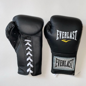 May include: A pair of black Everlast boxing gloves. One glove is laced with white laces. The other glove features the Everlast logo in white with a yellow accent. The gloves are made of leather.