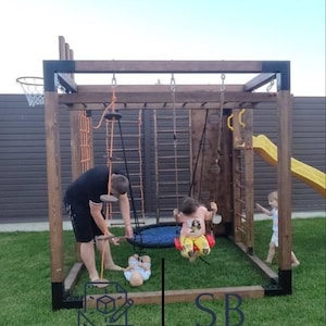May include: A wooden outdoor playground structure featuring a dark brown frame with black metal corner brackets, a rope ladder, a climbing wall, a yellow slide, a basketball hoop, and two hanging swings, with text reading SB PLAYGROUND WORLD.