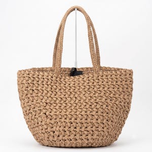 Può includere: Una borsa tote beige caratterizzata da una costruzione a maglia aperta intrecciata con un aspetto testurizzato. La borsa presenta due manici intrecciati abbinati fissati al bordo superiore e una base ampia e arrotondata, dalla forma strutturata.