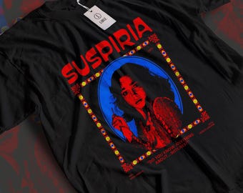 Puede incluir: Camiseta negra con la palabra "SUSPIRIA" en rojo, y un retrato de una mujer en un marco ovalado azul. La camiseta también incluye el texto "DO YOU KNOW ANYTHING ABOUT...WITCHES?" y "JESSICA HARPER".