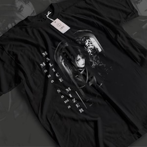 Puede incluir: Camiseta negra con un gráfico en escala de grises de una persona con pelo largo y elementos góticos. El texto "MALICE MIZER" está impreso verticalmente. Una etiqueta blanca con "LARGE" está adjunta.