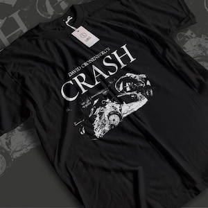 May include: Black t-shirt with the white text "DAVID CRONENBERG'S CRASH" and a grayscale image of a car crash. A white tag with "LARGE" is attached. The shirt is a Large size.