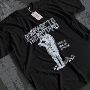 Puede incluir: Camiseta negra con un diseño gráfico blanco. El diseño incluye el texto "DISGRACE TO THE BASTARD" sobre una figura esbozada y las palabras "NEGATIVE DRINKING ATTITUDE". Una etiqueta blanca dice "LARGE".