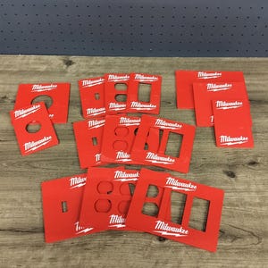 May include: A collection of red Milwaukee electrical outlet covers and faceplates. The covers have various cutouts for outlets and switches. The Milwaukee logo is printed in white on each piece. The items are arranged on a wooden surface.