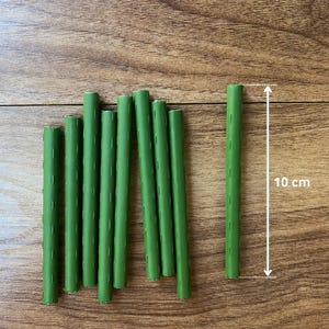 Peut inclure: Plusieurs bigoudis verts, chacun d'environ 10 cm de long, disposés sur une surface en bois. Les bigoudis sont cylindriques avec de petites fentes verticales. Un bigoudi mesure 10 cm de long.