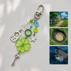 May include: A keychain featuring a silver lobster clasp, a rectangular tag with the text "YOU ARE MY ONLY" and a clover cutout, a large translucent green clover charm, a silver key charm with "Love" engraved, and various blue and green buttons.