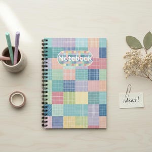 Puede incluir: Un cuaderno con espiral con un diseño de patchwork colorido. La portada presenta una cuadrícula de cuadrados pastel en tonos azules, rosas, amarillos y verdes. La palabra "Notebook" está impresa en la portada. También se ven bolígrafos, una taza pequeña y cinta adhesiva.
