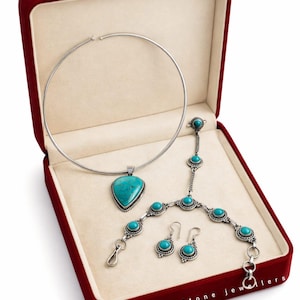 Könnte beinhalten: Ein Schmuckset in einer roten Samtbox. Das Set beinhaltet eine silberne Halskette mit einem türkisfarbenen Anhänger, ein Armband, Ohrringe und eine Handkette, alle mit türkisfarbenen Steinen. Der Text "Rakhi Jemstone Jewellers" ist sichtbar.
