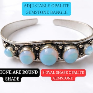 May include: An adjustable silver bangle featuring three oval-shaped opalescent gemstones and two round side stones. The bangle has a decorative design around the gemstones and is open-ended.