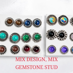 Op de afbeelding: Een verzameling edelsteen oorknopjes in verschillende kleuren, waaronder groen, rood, blauw en paars. Elke oorbel heeft een zilverkleurige, decoratieve rand. De tekst "MIX DESIGN, MIX GEMSTONE STUD" wordt in het rood weergegeven.