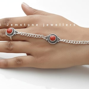 Puede incluir: Pulsera de cadena de mano plateada con un anillo, conectada por una cadena. La pulsera y el anillo presentan piedras preciosas rojas redondas engastadas en engastes plateados ornamentados. El texto "Rakhi Jemstone jewellers" es visible.