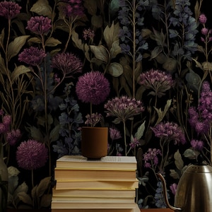 Könnte beinhalten: Dunkle florale Tapete mit lila und grünen botanischen Illustrationen. Ein Stapel Bücher mit vergilbten Seiten und eine braune Keramiktasse stehen auf einer Holzoberfläche. Ein silberner Wasserkocher ist ebenfalls zu sehen.