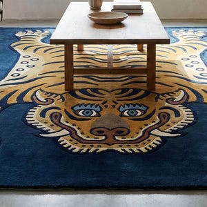 May include: A large, rectangular rug with a tiger design. The rug features a navy blue background with a detailed tiger illustration in shades of tan, cream, and brown. The tiger's face and body are prominently displayed.