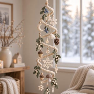 May include: A spiral-shaped hanging decoration made of cream-colored crochet yarn. It features various crocheted ornaments including green leaves, blue berries, white snowflakes, a crescent moon, brown pinecones, acorns, and a small mushroom.