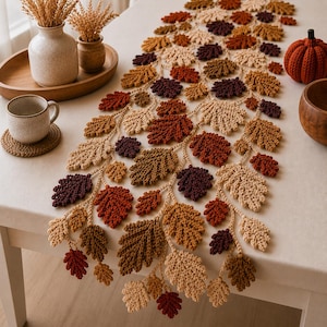May include: A crochet table runner featuring a repeating pattern of oak leaves in shades of cream, tan, rust orange, and deep burgundy. The leaves are connected by a central crocheted vine structure, creating a long, decorative autumn-themed piece.